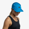 Una mujer con una camiseta Jockey Buff Pack Speed HTR azul brillante y una camiseta negra sin mangas mira hacia abajo sobre un fondo blanco liso, con el cabello atado en una cola de caballo.