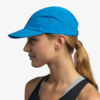 Una persona con cabello largo recogido en una cola baja viste una gorra Jockey Buff Pack Speed HTR (copia) azul y una camiseta deportiva sin mangas, mirando hacia la izquierda con una expresión neutra sobre un fondo blanco liso.