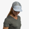 Una persona con cabello largo viste una gorra Jockey Buff Speed Lilac Shane y una camisa gris de manga corta, exudando calma mientras mira hacia abajo sobre un fondo blanco liso.