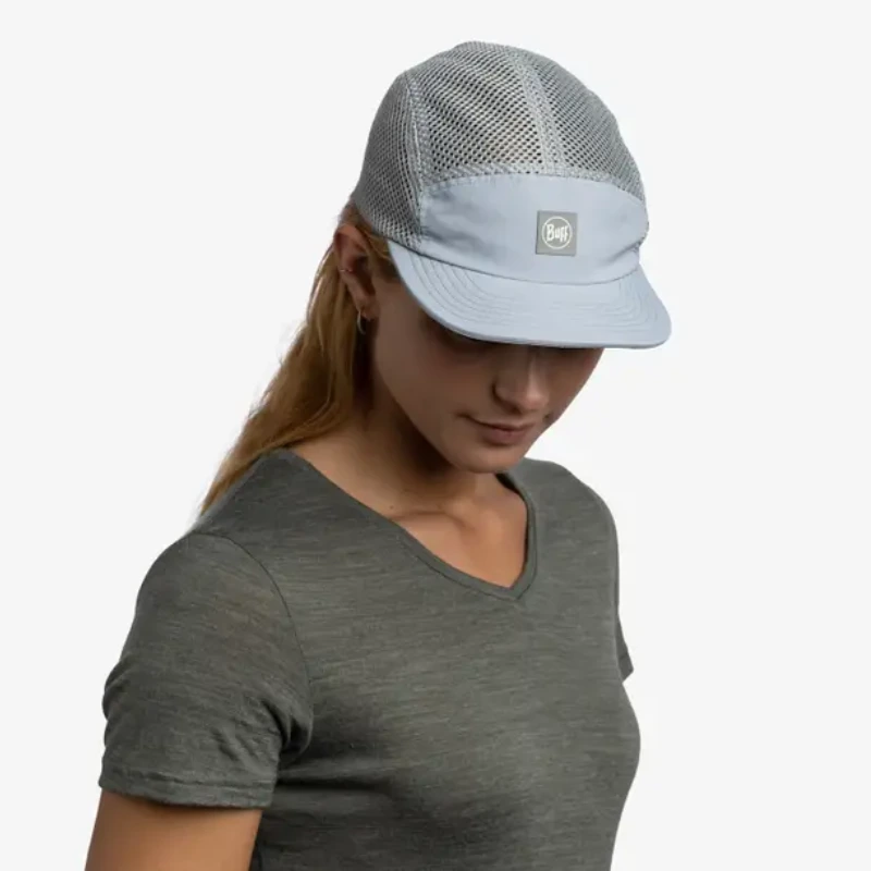 Una persona con cabello largo viste una gorra Jockey Buff Speed Lilac Shane y una camisa gris de manga corta, exudando calma mientras mira hacia abajo sobre un fondo blanco liso.
