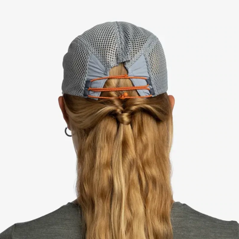 La vista posterior muestra a una persona con cabello rubio largo que fluye a través de una gorra de malla gris con tiras naranjas, con un estilo sencillo como el de Shane. Su camisa gris realza el estilo deportivo del conjunto Jockey Buff Speed Lilac Shane (copia).