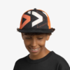 Una persona con una camisa negra y una gorra de béisbol Jockey Buff Niños Baseball Arrows Denim con patrones geométricos abstractos en naranja, rojo y blanco sonríe mientras mira hacia abajo sobre un fondo blanco.
