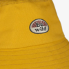 Primer plano de un sombrero de pescador amarillo, similar al estilo vibrante del Jockey Buff Niños 5 Panel Go Black Noru. Tiene un parche bordado que presenta un diseño de semicírculo rojo y blanco con la palabra "be wild" en negro, lo que resalta sus costuras visibles como un accesorio llamativo.