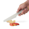 Una mano maneja hábilmente un cuchillo del Set de Cocina 4pc Sea To Summit Frontier (copia), cortando sin esfuerzo una manzana roja, dejando rebanadas finas y perfectas artísticamente distribuidas sobre una superficie liviana.