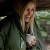 Acurrucada en un saco de dormir, la mujer de larga melena rubia sonríe radiante mientras sostiene una taza de Sea To Summit Detour. En su tienda de campaña, rodeada de árboles tranquilos, captura la alegría de las aventuras al aire libre.