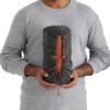 Una persona que viste una camisa gris de manga larga sostiene una bolsa cilíndrica compacta con cordón y un interior naranja vibrante, ideal para aventuras al aire libre y con el tamaño perfecto para adaptarse a una Colchoneta Autoinflable Sea to Summit Pursuit Plus (copia).