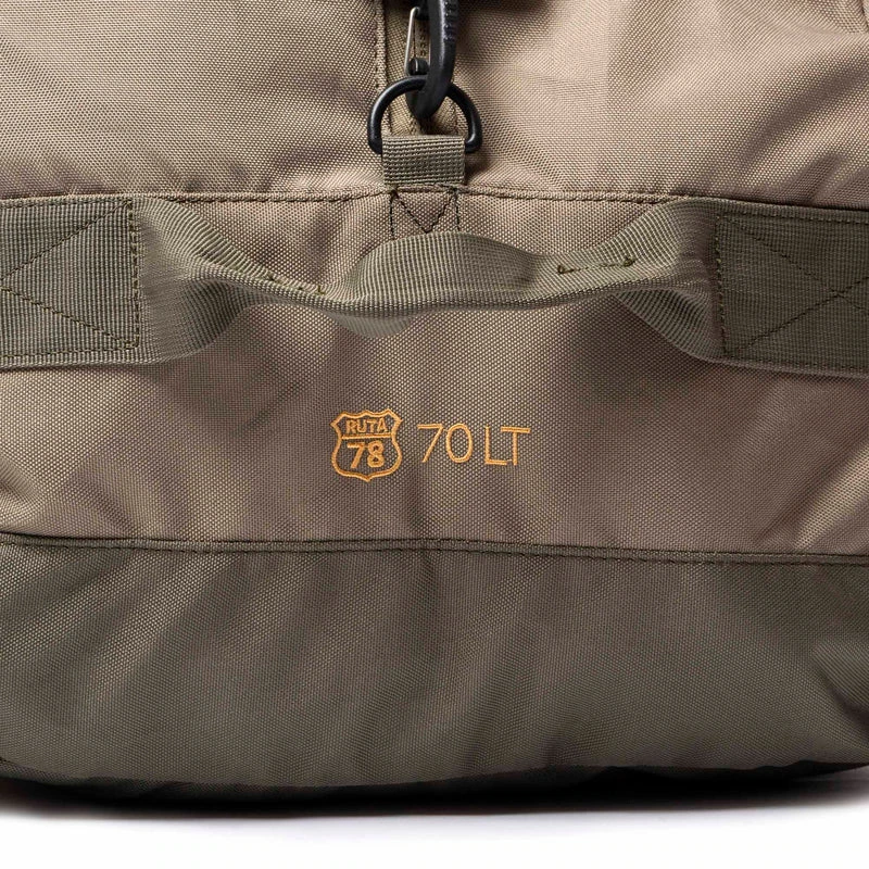 Primer plano de una mochila color caqui con un parche con el emblema de la Ruta 78 y el texto "70 LT" en amarillo. La tela tiene costuras visibles y un asa de red sobre el parche.