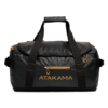 Se muestra una bolsa de lona negra con asas y cremalleras resistentes del mismo color. Luce la palabra "ATAKAMA" en negrita amarilla en el bolsillo frontal. La bolsa se presenta sobre un fondo blanco liso.