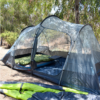 Una carpa Carpa Atakama Outdoor Totoralillo para 4 personas está instalada al aire libre bajo árboles altos, con dos camas inflables y colchonetas verdes en el interior. El área es seca, con hojas y ramas dispersas, y cerca hay una colchoneta plegable.