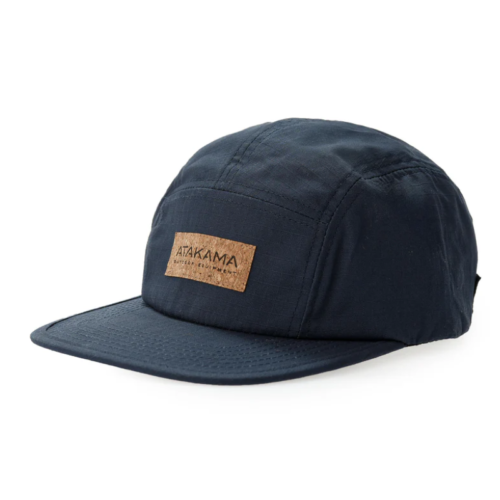 La gorra Jockey Atakama Outdoor Five Panel Puelo es azul marino con un parche de corcho en la parte frontal que dice "ATAKAMA". Presenta una visera plana y un diseño estructurado, ideal para aventureros con estilo que buscan estilo y funcionalidad.