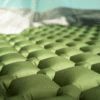 Primer plano de una Colchoneta Inflable Yerba Loca Kano verde con textura acolchada, instalada dentro de una carpa mientras la luz del sol se filtra a través de la tela.