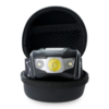 Una linterna frontal Atakama Outdoor Alma 195lm, con una luz amarilla central y luces laterales más pequeñas, se muestra en un estuche negro abierto con cremallera y un interior texturizado, ideal para los entusiastas del aire libre.