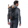Una persona de espaldas, con camisa gris de manga larga y pantalones oscuros, lleva una mochila plegable Atakama Outdoor Ruta 78 de 70 litros (copia). La mochila negra de senderismo contiene dos bastones de trekking y una cantimplora, lista para la aventura.