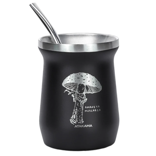 Una taza negra con borde metálico y pajita presenta a una persona sosteniendo un paraguas con forma de hongo. Debajo de la ilustración, se lee "Amanita Muscaria" y "Atakama". Captura el estilo campestre de Atakama, que recuerda a su colección de Botellas Térmicas Atakama Outdoor de 1 L.