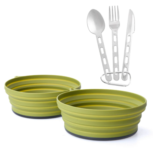 Dos cuencos plegables de silicona verde del Set de Cocina Atakama Outdoor Avellana se encuentran uno al lado del otro. Sobre ellos, un elegante juego de cubiertos de metal con cuchara, tenedor y cuchillo unidos por una anilla presenta elegantes mangos recortados. Perfecto para los amantes de la gastronomía aventurera.