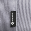 Un primer plano de una tela gris claro con nervaduras verticales, perfecta para las aventuras de Atakama Outdoor, con una etiqueta negra con la palabra "ATAKAMA" en texto blanco en negrita y un pequeño logotipo "P" circular, que recuerda al elegante diseño que se encuentra en la Toalla Microfibra Maullín.